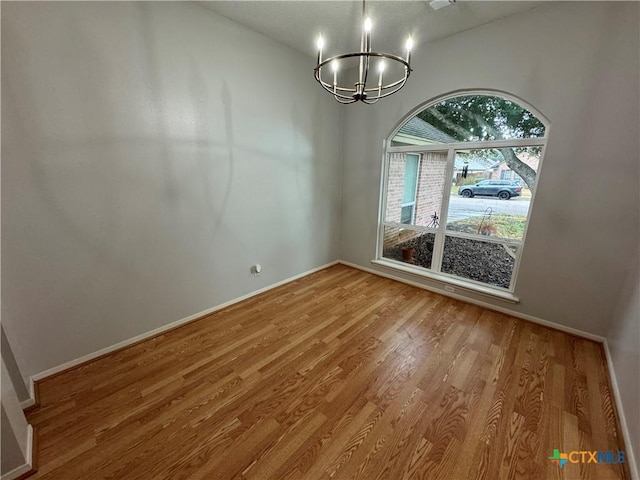 unfurnished dining area with baseboards, wood finished floors, and an inviting chandelier