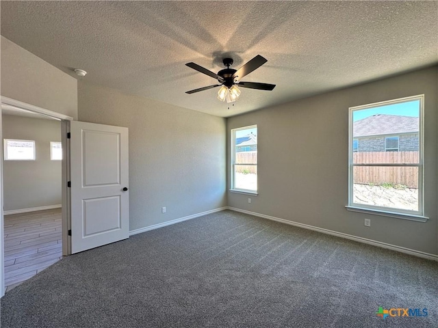 spare room with a textured ceiling, dark colored carpet, a ceiling fan, and baseboards