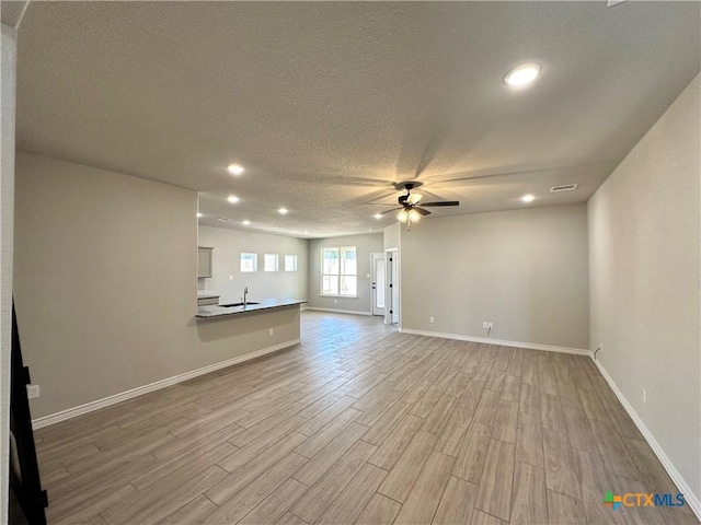 unfurnished living room with ceiling fan, wood finished floors, recessed lighting, baseboards, and a textured ceiling
