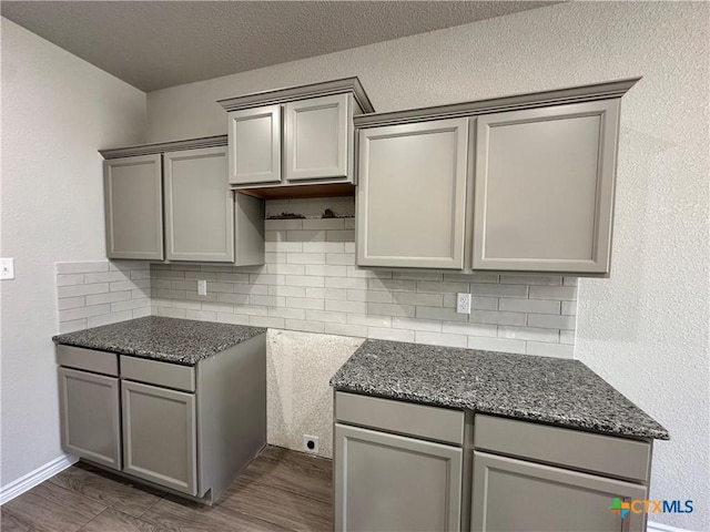 kitchen featuring backsplash, gray cabinetry, dark stone countertops, and dark wood-style floors