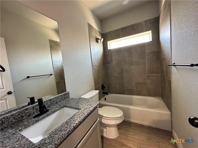 bathroom featuring a textured wall, wood finished floors, toilet, shower / tub combination, and vanity