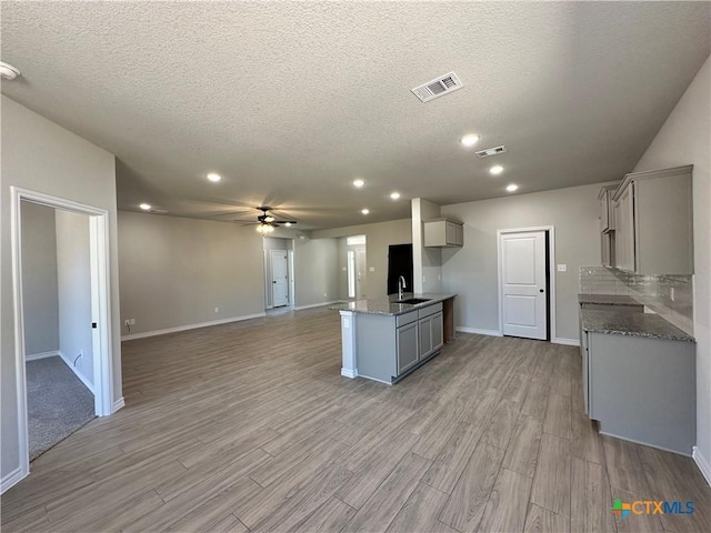 kitchen featuring gray cabinetry, open floor plan, ceiling fan, light wood finished floors, and a textured ceiling