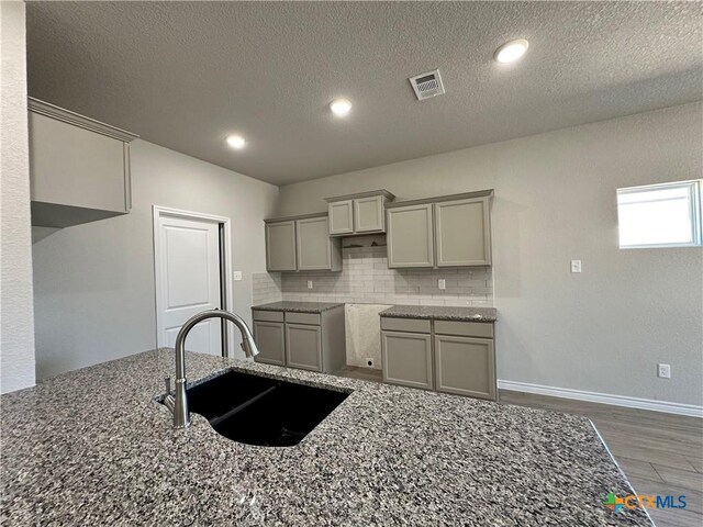 kitchen with a sink, stone counters, gray cabinetry, backsplash, and wood finished floors