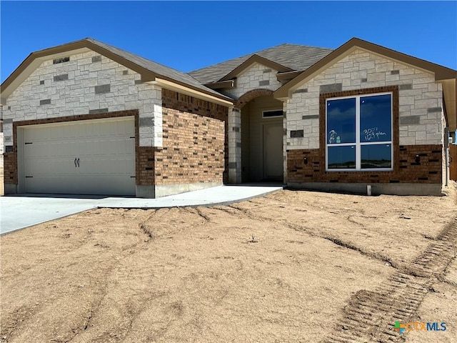 view of front of property featuring a garage, driveway, stone siding, and brick siding