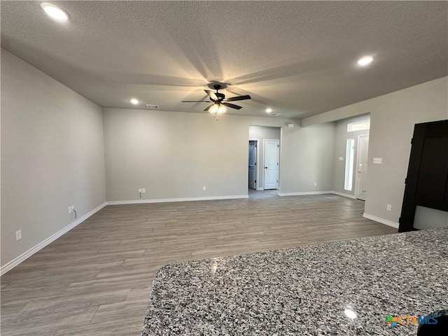 empty room with a ceiling fan, wood finished floors, a textured ceiling, recessed lighting, and baseboards