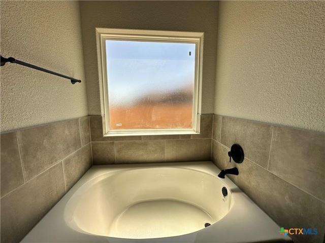 bathroom with plenty of natural light, a bath, and a textured wall