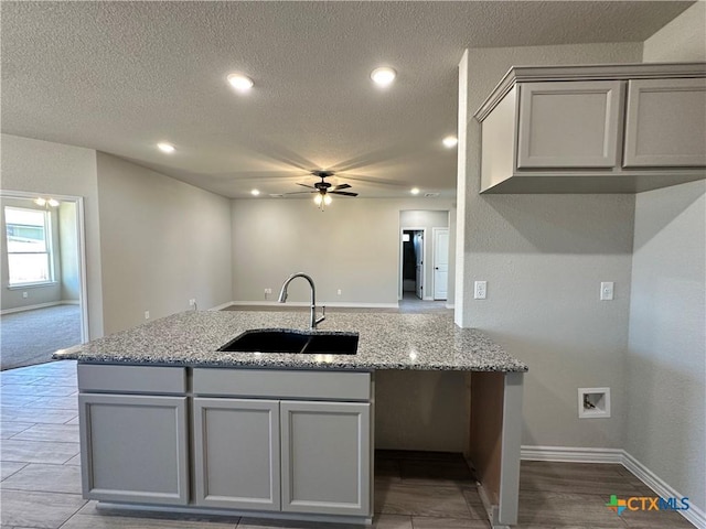 kitchen featuring a sink, gray cabinets, ceiling fan, baseboards, and light stone countertops