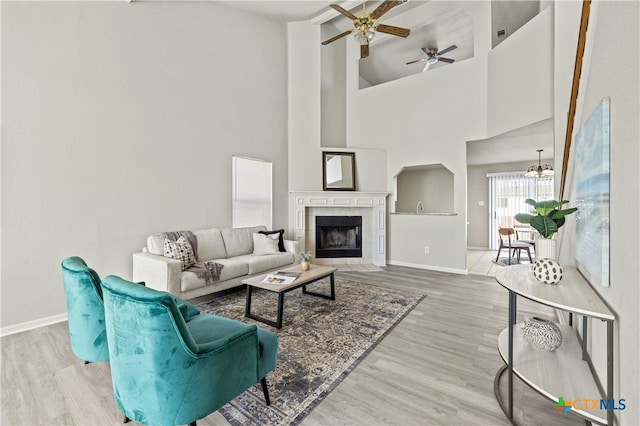 living room featuring a tile fireplace, hardwood / wood-style floors, a high ceiling, and ceiling fan with notable chandelier