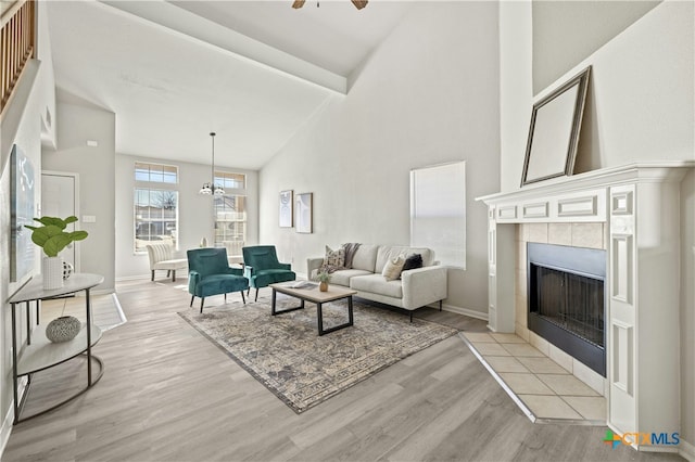 living room featuring a tile fireplace, ceiling fan, a towering ceiling, and light wood-type flooring