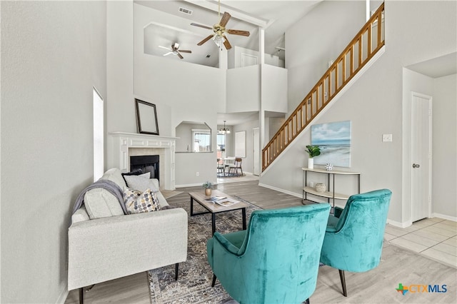 living room with ceiling fan with notable chandelier, a high ceiling, and light hardwood / wood-style flooring