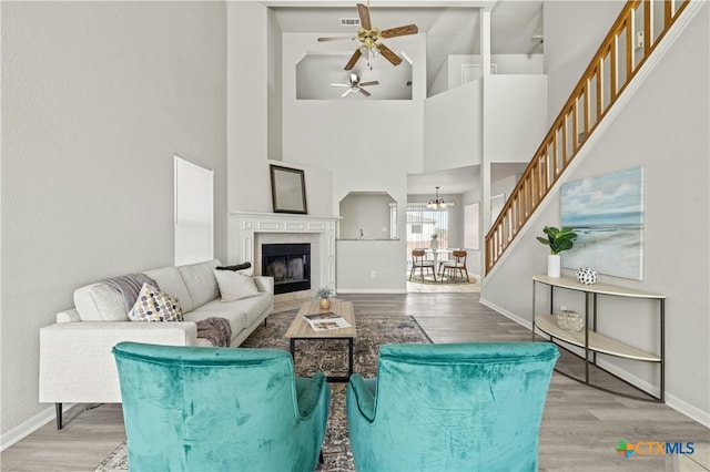 living room featuring ceiling fan with notable chandelier, light wood-type flooring, a tile fireplace, and a high ceiling