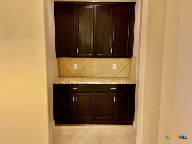 kitchen with dark brown cabinets, light tile patterned floors, light stone counters, and decorative backsplash