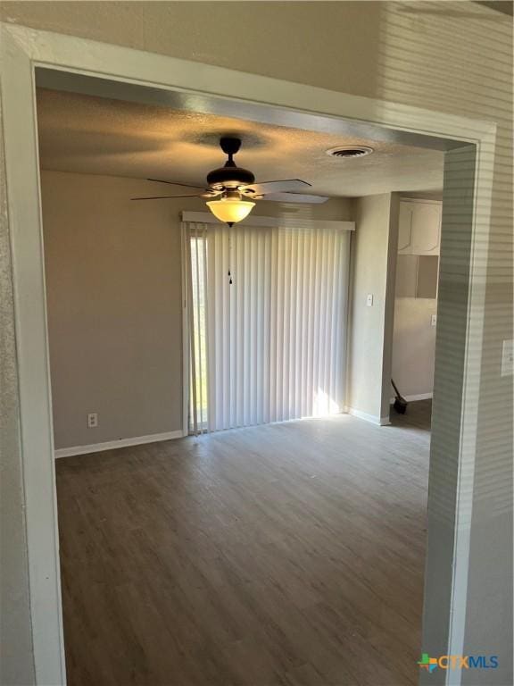 unfurnished room with dark wood-style floors, visible vents, ceiling fan, and baseboards