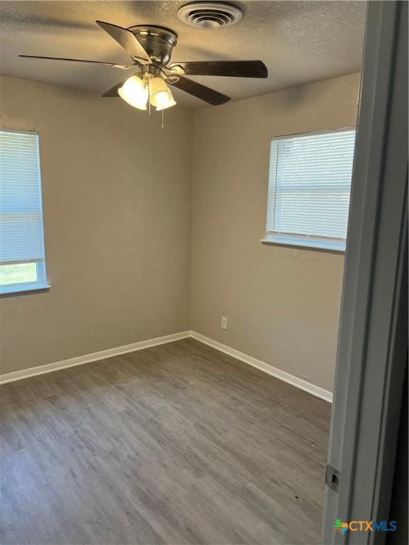 empty room with a textured ceiling, dark wood-type flooring, a ceiling fan, visible vents, and baseboards