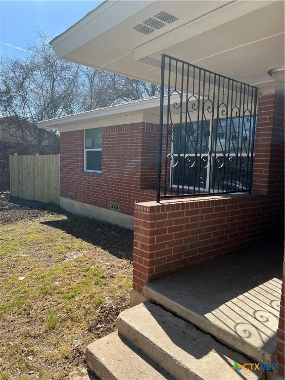 view of side of home featuring brick siding, crawl space, and fence