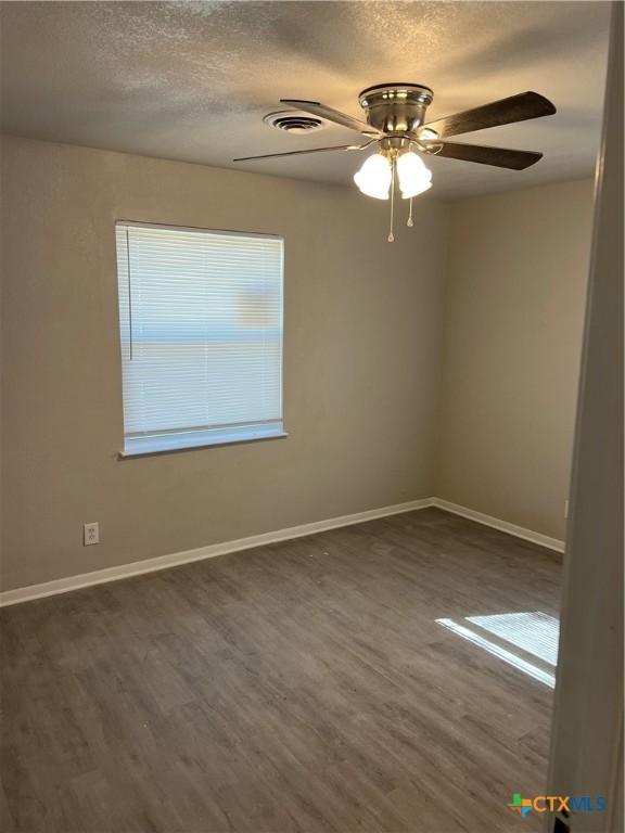 unfurnished room featuring visible vents, a ceiling fan, a textured ceiling, wood finished floors, and baseboards