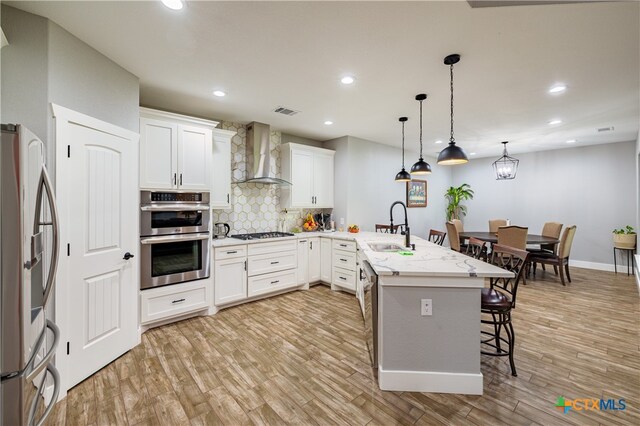 200 Wood Cv, Georgetown, TX 78633 - kitchen with wall chimney range hood, a sink, stainless steel appliances, a peninsula, and a kitchen breakfast bar
