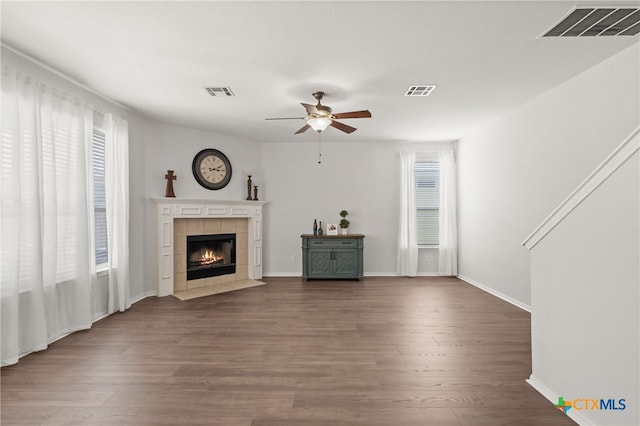 unfurnished living room featuring ceiling fan, a tiled fireplace, and dark hardwood / wood-style flooring