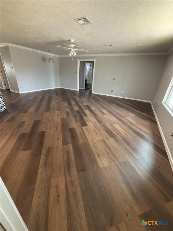 unfurnished living room with baseboards, visible vents, dark wood finished floors, ornamental molding, and a textured ceiling