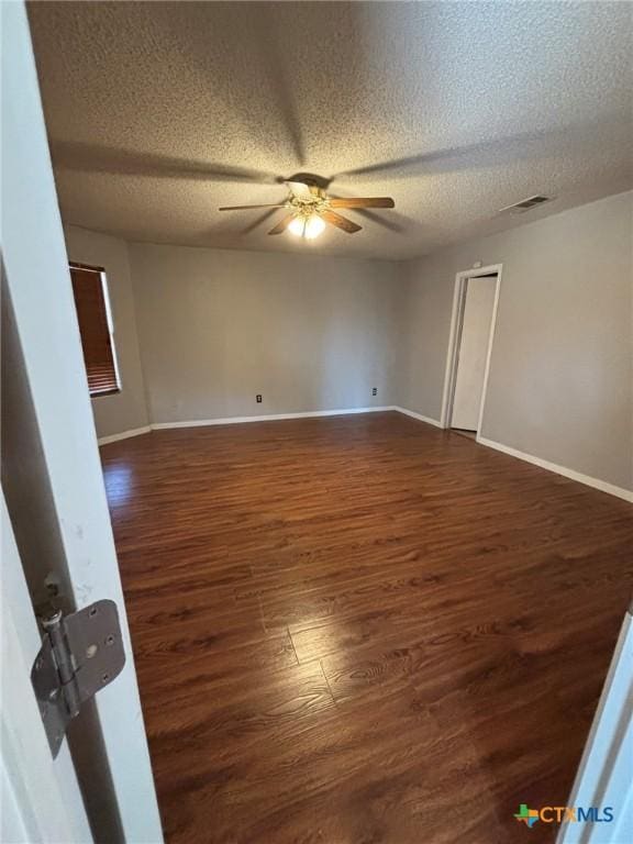 empty room with visible vents, dark wood-type flooring, a ceiling fan, a textured ceiling, and baseboards