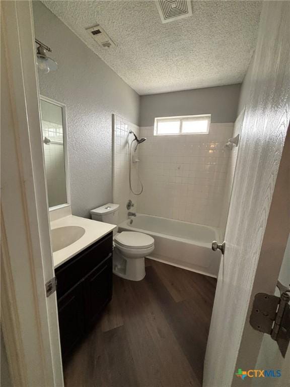 bathroom featuring wood finished floors, visible vents, a textured ceiling, bathing tub / shower combination, and a textured wall