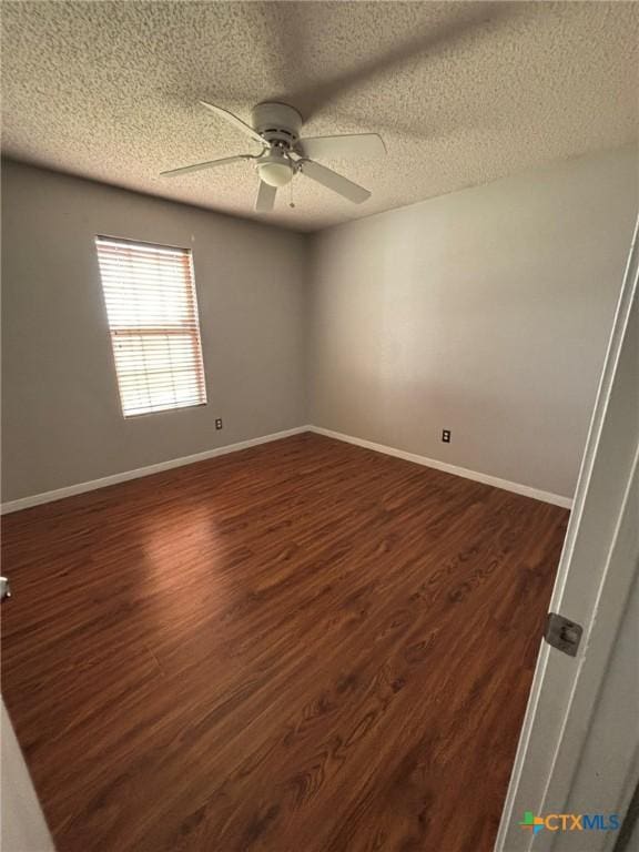 empty room with ceiling fan, a textured ceiling, dark wood-type flooring, and baseboards