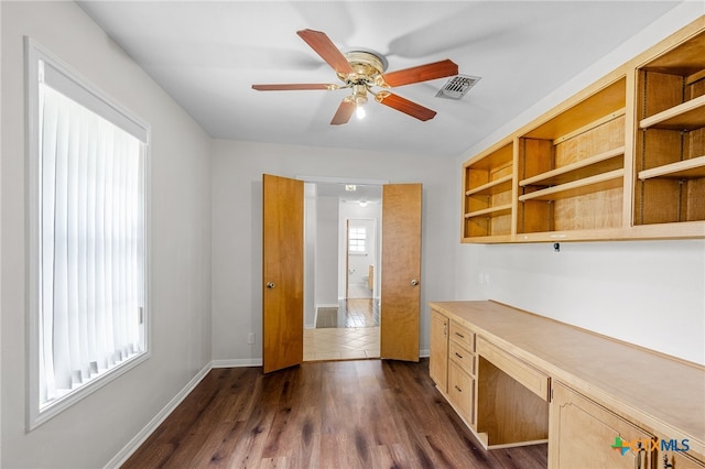 unfurnished office with dark hardwood / wood-style flooring, built in desk, ceiling fan, and plenty of natural light