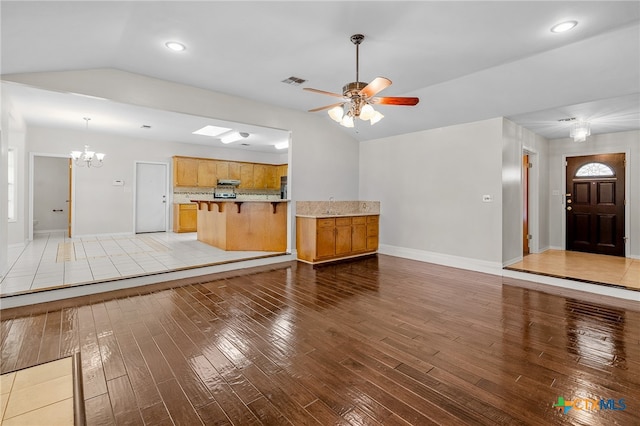 unfurnished living room with ceiling fan with notable chandelier, light wood-type flooring, and lofted ceiling with skylight