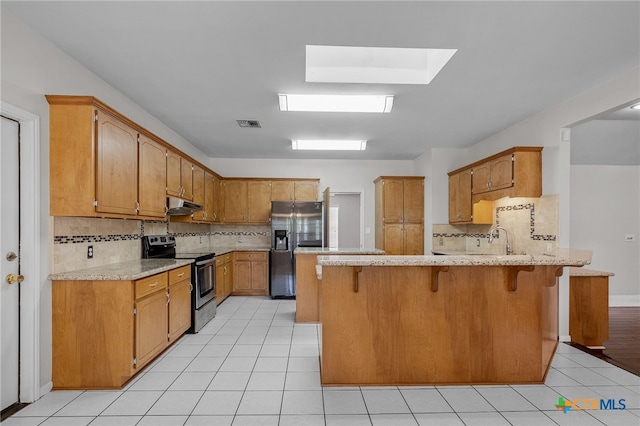 kitchen with a kitchen bar, light tile patterned floors, backsplash, and appliances with stainless steel finishes