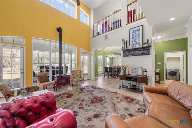 living room featuring a high ceiling, an inviting chandelier, a wood stove, washer / dryer, and crown molding