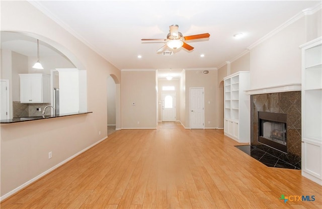 1935 Grandview Dr, Salado, TX 76571 - unfurnished living room with a ceiling fan, light wood-style floors, a tile fireplace, arched walkways, and crown molding