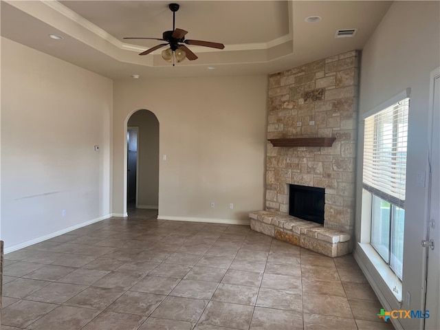 unfurnished living room featuring a raised ceiling, ceiling fan, a fireplace, and ornamental molding