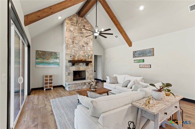 living room with high vaulted ceiling, a stone fireplace, ceiling fan, beamed ceiling, and light hardwood / wood-style floors