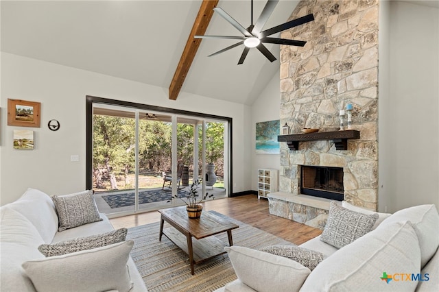 living room featuring ceiling fan, beam ceiling, hardwood / wood-style flooring, high vaulted ceiling, and a stone fireplace