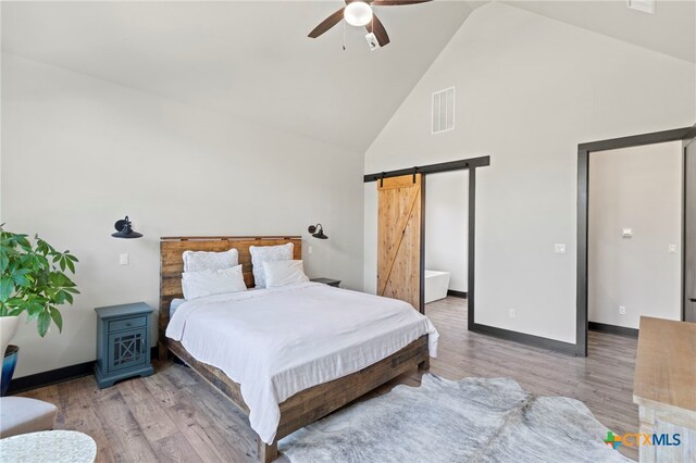 bedroom with a barn door, ceiling fan, high vaulted ceiling, and light hardwood / wood-style floors