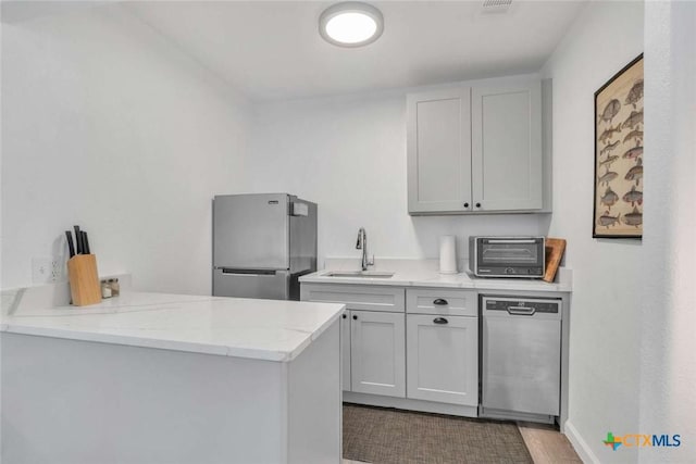 kitchen with a toaster, light stone counters, appliances with stainless steel finishes, a peninsula, and a sink