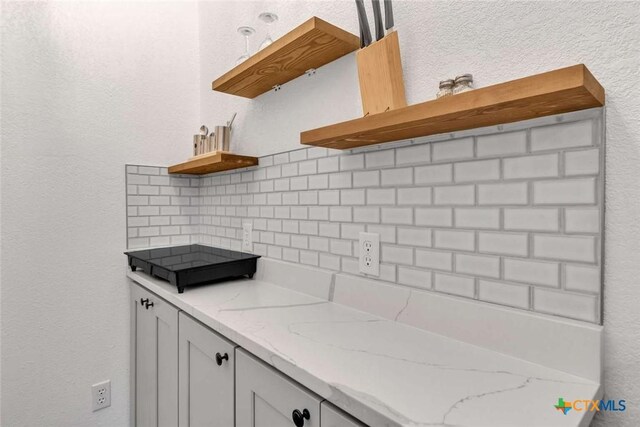 kitchen featuring light stone counters, backsplash, and open shelves