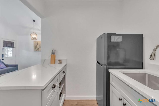 kitchen featuring light wood-style flooring, a sink, white cabinetry, freestanding refrigerator, and a peninsula