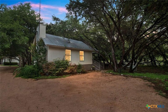 property exterior at dusk featuring a chimney and metal roof