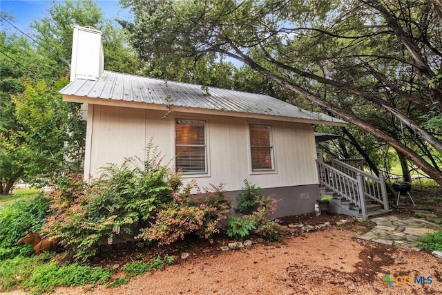 view of home's exterior featuring crawl space, a chimney, and metal roof