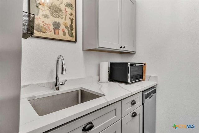 kitchen with a sink, light stone countertops, dishwasher, and a toaster