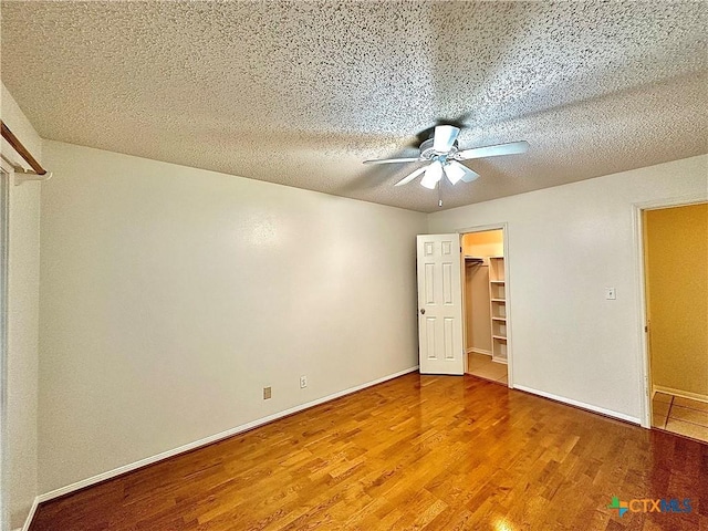 unfurnished bedroom featuring a walk in closet, ceiling fan, a textured ceiling, wood-type flooring, and a closet