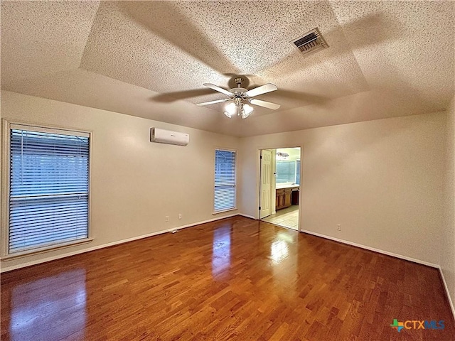 empty room with a textured ceiling, ceiling fan, light hardwood / wood-style floors, and a wall mounted air conditioner