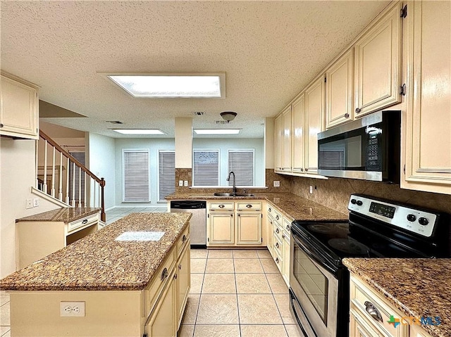 kitchen with sink, light tile patterned floors, a textured ceiling, appliances with stainless steel finishes, and a kitchen island