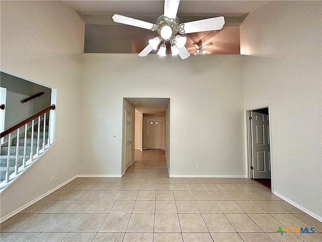 tiled spare room with ceiling fan and a towering ceiling