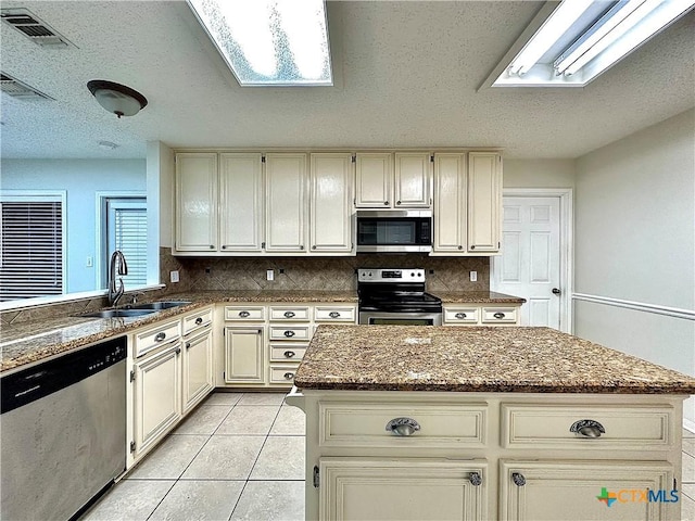 kitchen with appliances with stainless steel finishes, a center island, cream cabinets, and sink