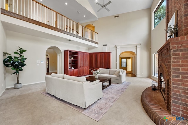 carpeted living room with a brick fireplace, a towering ceiling, and ceiling fan