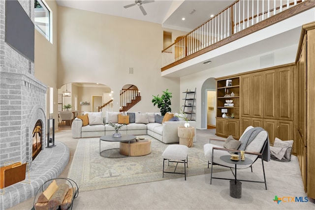 carpeted living room featuring a brick fireplace, ceiling fan, and a high ceiling