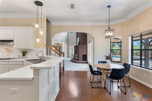 kitchen with white cabinets, hanging light fixtures, sink, exhaust hood, and a fireplace