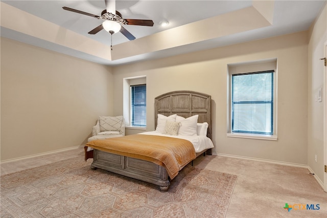 carpeted bedroom with ceiling fan and a tray ceiling